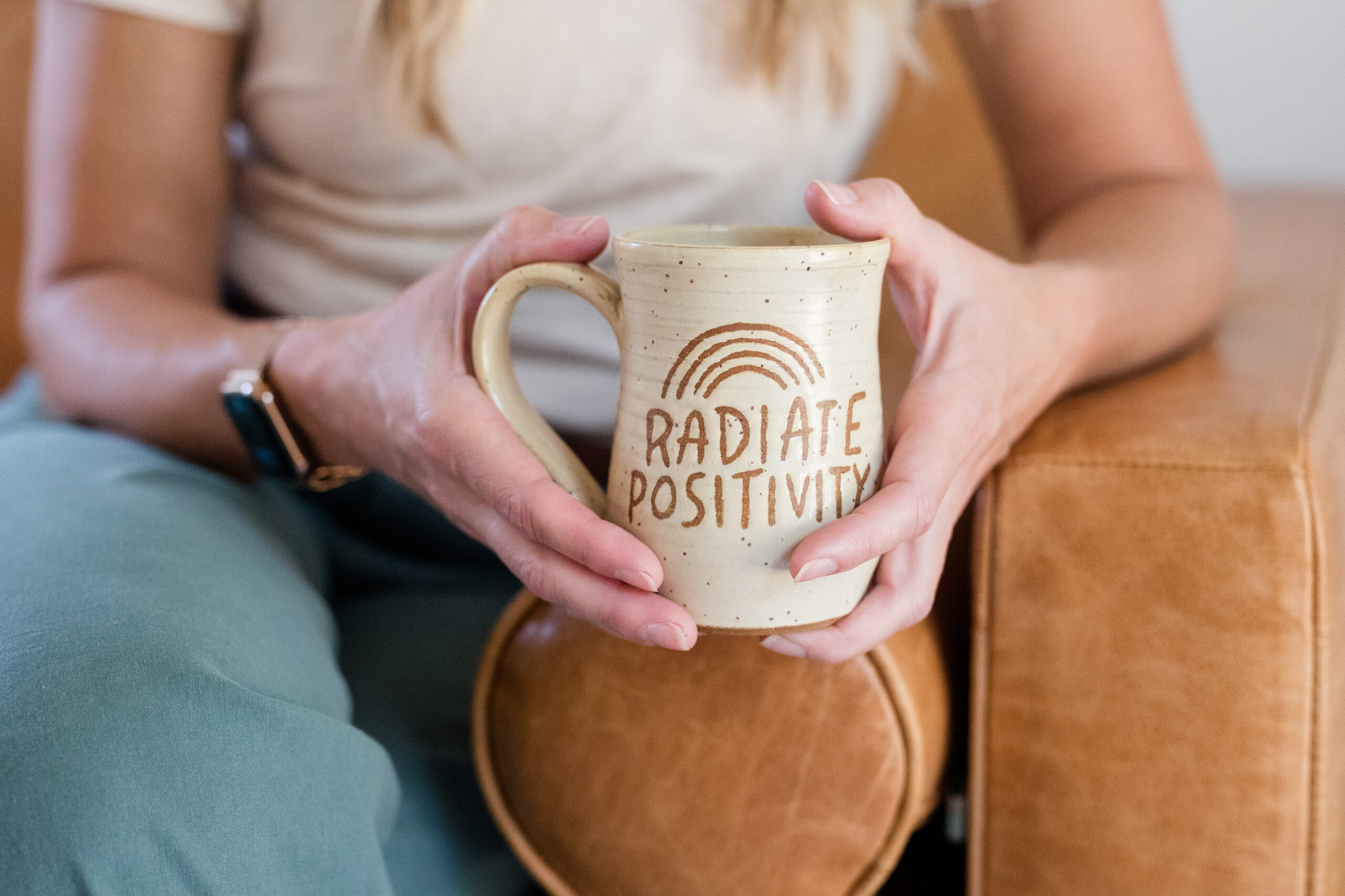 Amy sitting in a a chair holding a mug that says "Radiate Positivity"