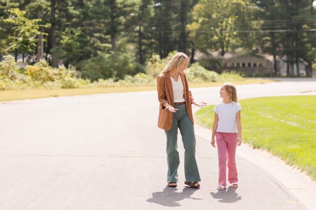 Parent and child walking side by side outdoors on a sunny path.